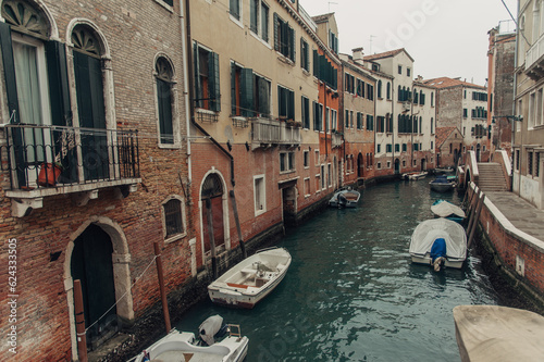A picturesque Venice canal with boats lining the water, charming houses on one side, and a bridge with a sidewalk on the other. © Alejandro