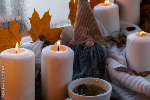 Thanksgiving and Hello Fall Halloween concept Celebrating autumn holidays at cozy home on the windowsill Hygge aesthetic atmosphere Autumn leaves gnome, spices and candle on knitted white sweater in