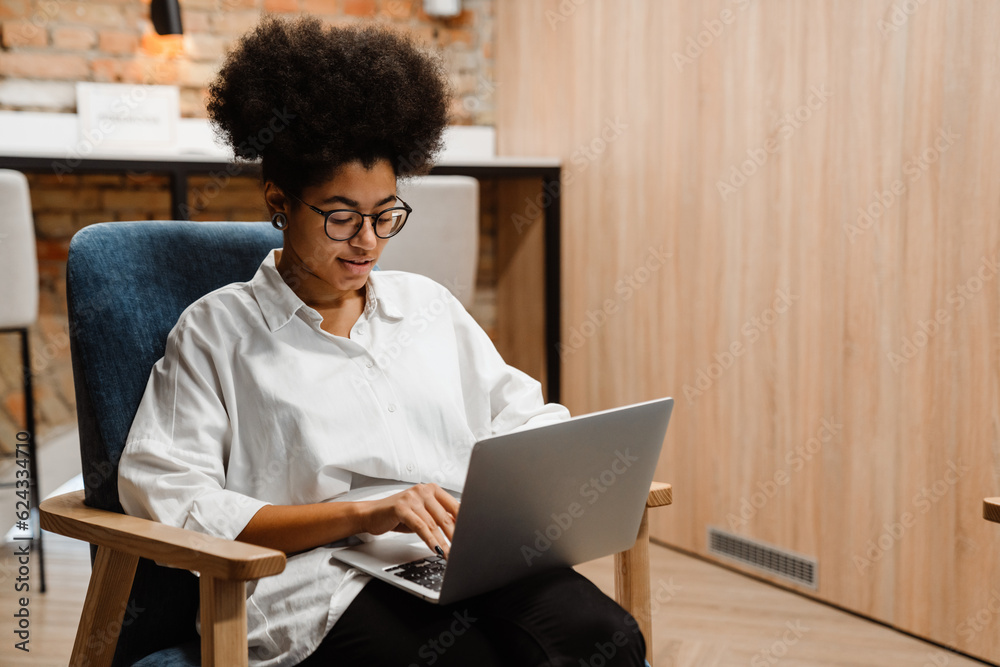 African woman working on laptop while sitting in office African woman working on laptop while sitting in office