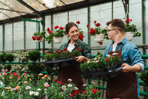 Woman florist and man with down syndrome taking care of flowers in greenhouse photo