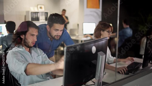 Coworkers looking at a computer and talking about work. Team of colleagues brainstorming together while working on the computer. Men colleagues discuss online project look at pc screen