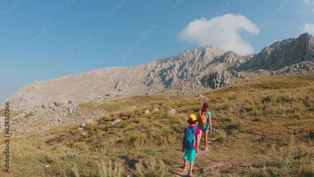 Hiking in the mountains. A woman and a child are walking along a mountain path. A boy with a backpack travels with his mother. Hiking with children. The kid goes along the mountain range. Hiking in the mountains. A woman and a child are walking along a mountain path. A boy with a backpack travels with his mother. Hiking with children. The kid goes along the mountain range.