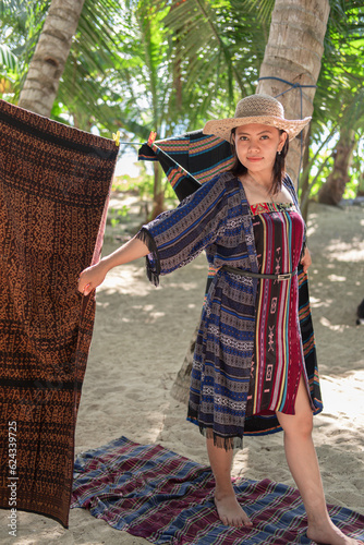 A young Asian woman wearing traditional clothes made of woven cloth combined with batik cloth with a tree background 