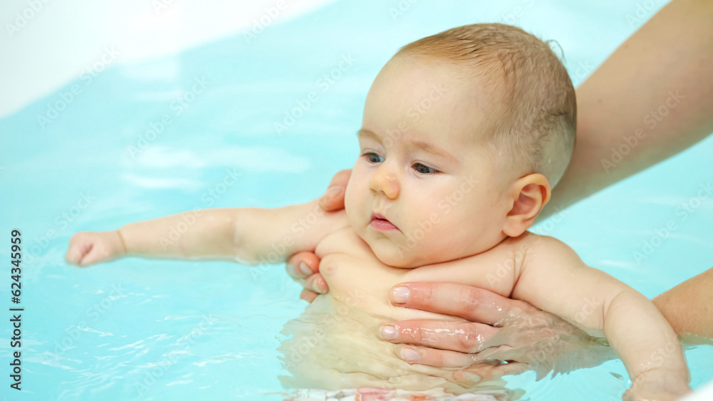 Swim teacher holds baby under arms and girl swings legs in bathtub. Newborn girl face expresses happiness and joy from swimming process Swim teacher holds baby under arms and girl swings legs in bathtub. Newborn girl face expresses happiness and joy from swimming process