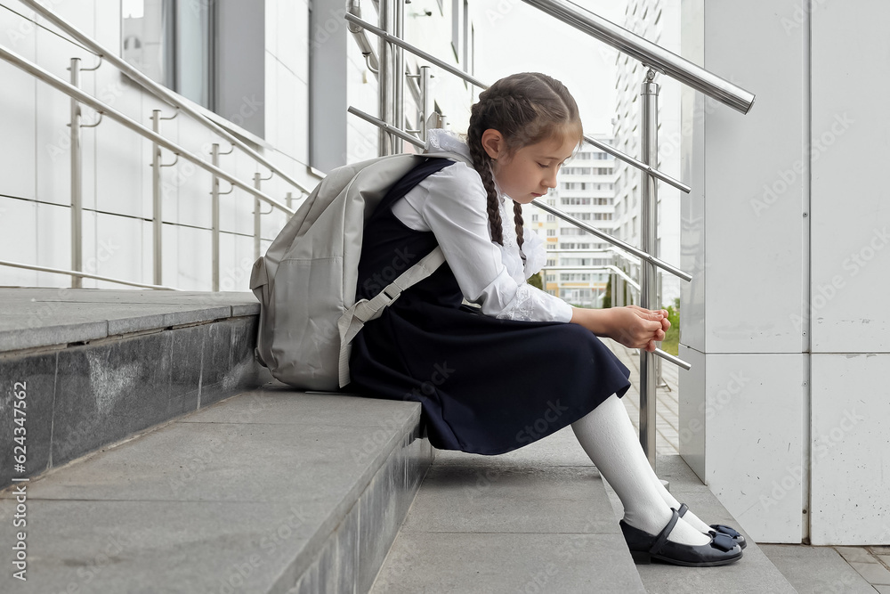 Junior schoolgirl sits with sad expression. Girl with long braids afraid to attend school and see bullies Junior schoolgirl sits with sad expression. Girl with long braids afraid to attend school and see bullies