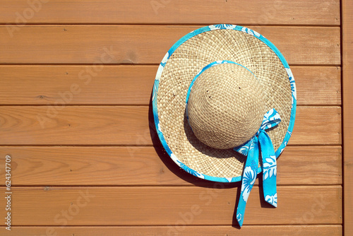 Sandy brown rustic straw female hat with decorative flowers hangs on wooden wall as background front view