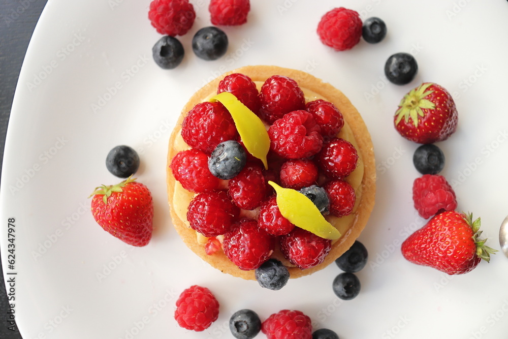 cream cake with raspberries and blueberries and small macaroons served on a large white plate cream cake with raspberries and blueberries and small macaroons served on a large white plate