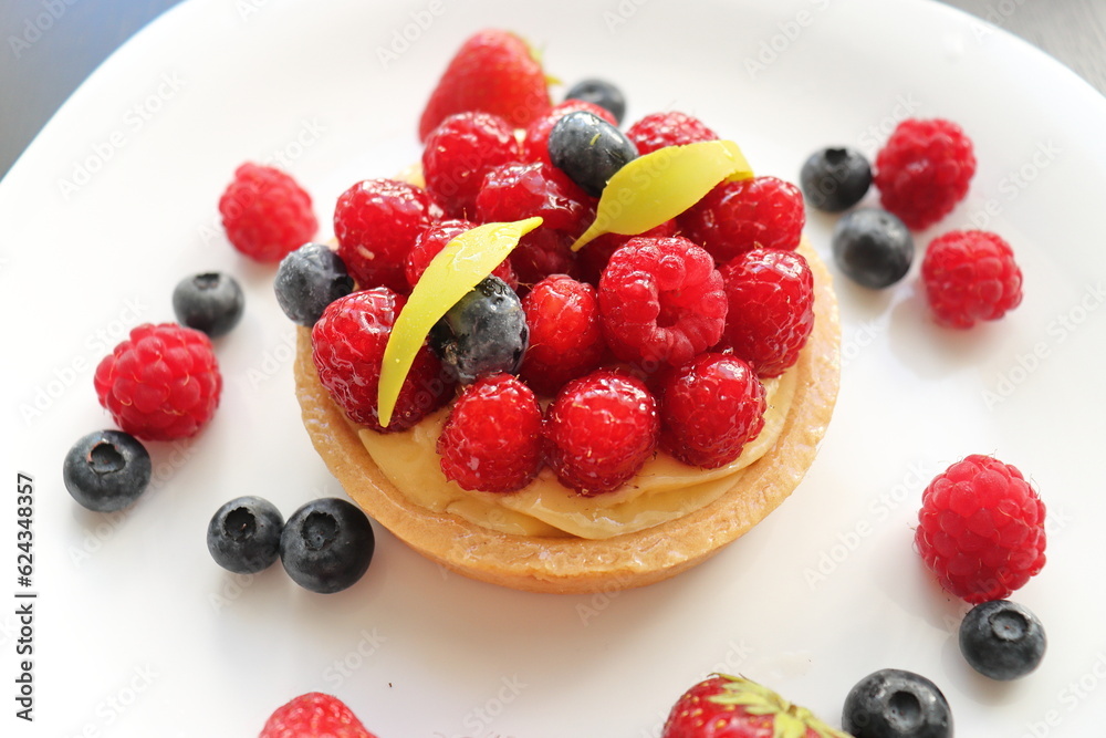 cream cake with raspberries and blueberries and small macaroons served on a large white plate