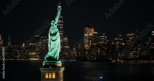 Panoramic Aerial Footage of an American Symbol of Freedom. Cinematic Helicopter Pass by the Statue of Liberty at Night. Landmark New York Monument with Manhattan Skyscrapers in the Background