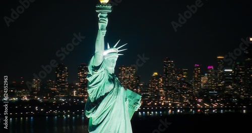 Aerial View of the Illuminated Statue of Liberty. Iconic Travel Destination and Tourist Attraction with Manhattan and Brooklyn Office Buildings with Lights at Night. Midnight Scenes of New York City