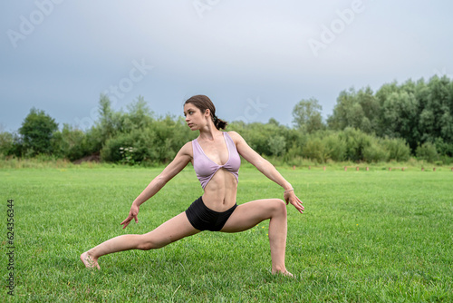 Portrait of young fitness trainer practicing pilates exercise in quit summer park, morning time