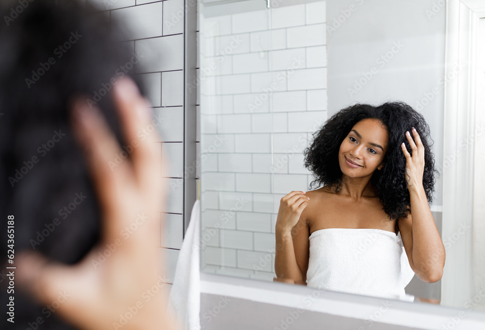 Smiling female looking at her reflection in a mirror and adjusting her hair Smiling female looking at her reflection in a mirror and adjusting her hair