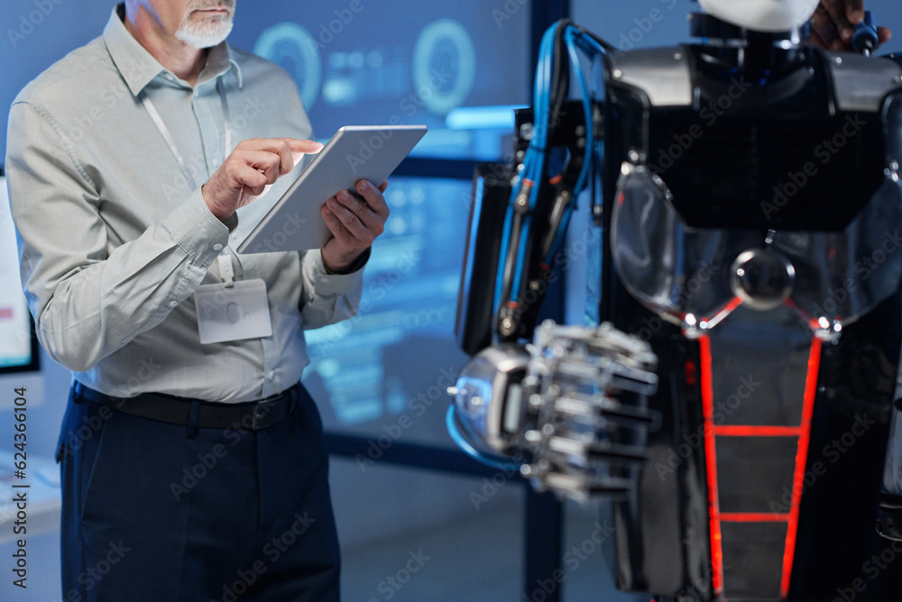 Close-up of mature engineer using digital tablet to connect with robot during his work in the lab Close-up of mature engineer using digital tablet to connect with robot during his work in the lab