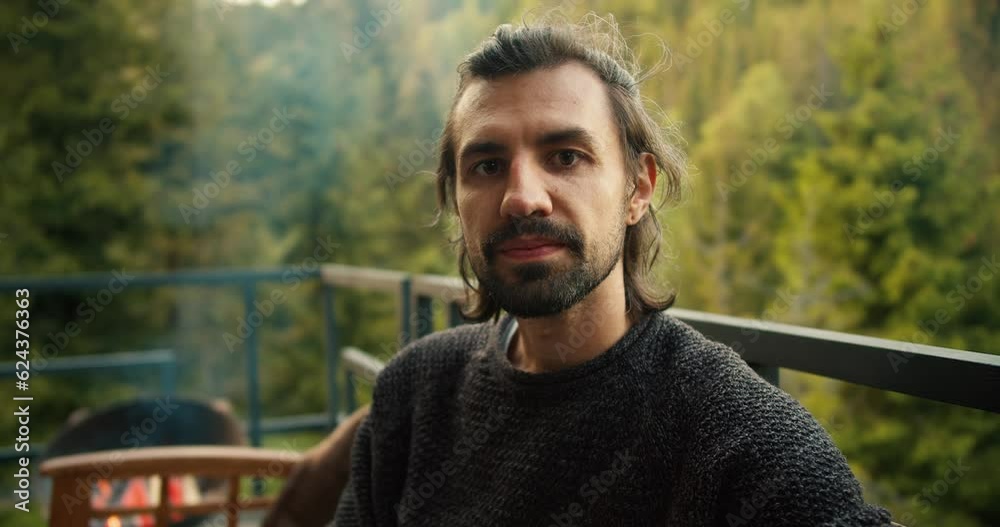Portrait of a serious young man at a picnic outside the city. Overview of a guy who is sitting on a devan with a view of the mountains and coniferous forest