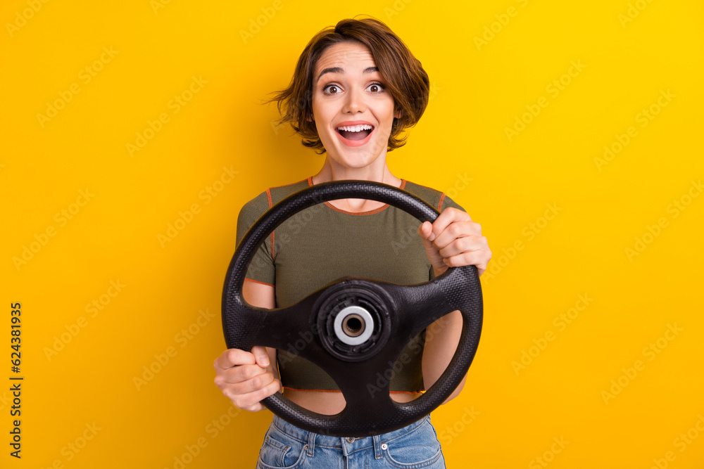 Photo of satisfied impressed nice girl dressed khaki t-shirt holding steering wheel buy new car isolated on yellow color background Photo of satisfied impressed nice girl dressed khaki t-shirt holding steering wheel buy new car isolated on yellow color background