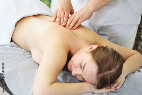 masseur massages the back, lower back, shoulders and neck of a young woman against the background of a bright office and greenery.