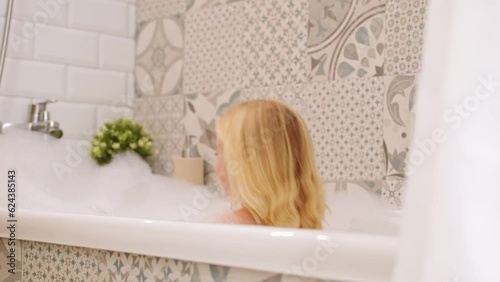 Cute funny caucasian blonde three years old girl taking bath with white foam bubbles, playing,smiling , having fun.Carefree childhood, kid body care concept.  photo