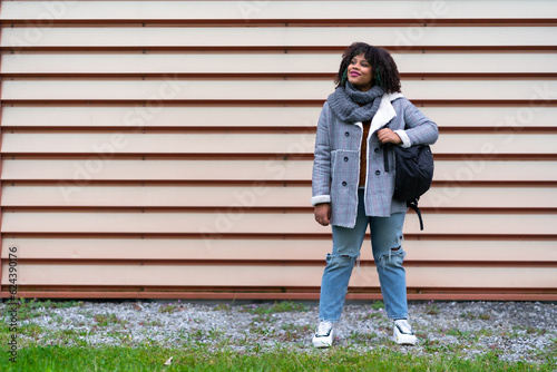 Portrait of black ethnic girl a gray wall in the university, with mochica from school on the back to school