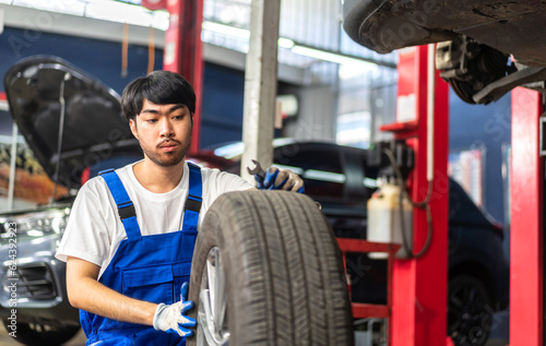 Professional car technician mechanic man in uniform work and maintenance repairing checking removing black wheel tire car before a long travel in auto service.Automobile service garage