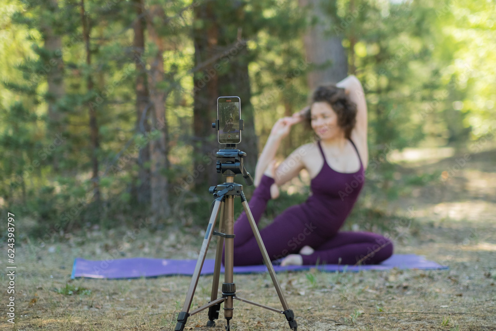 Young woman doing yoga in nature online using phone and application