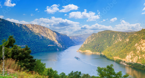 Amazing nature landscape of the Danube River. Tourist cruise ship passes by the gorge. Summer sky with clouds.