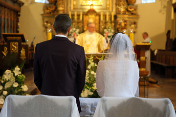 A young couple stands in front of the altar during a wedding ceremony in a Catholic church.