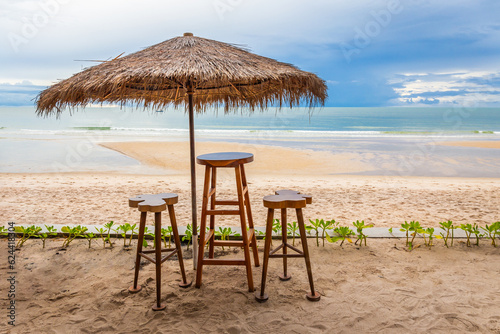 Fototapeta Naklejka Na Ścianę i Meble -  Set of wooden tables and chairs and leaf umbrellas for sitting and drinking drinks by the beach with sky and tide waves.