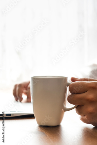 Office work on computer while drinking coffee in daylight