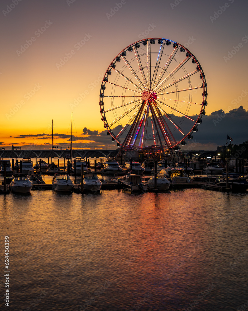 Illuminated ferris wheel at National Harbor near the nation capital of Washington DC at sunset with marina in the foreground