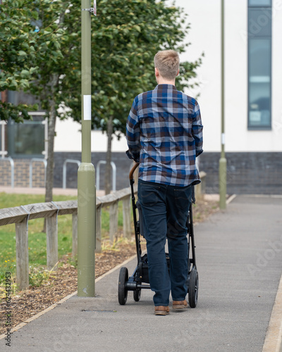 Young English father in plaid shirt walks with pram on summer day. Authentic, back view, urban parenting, family, happiness. Vertical crop. © Oleksandr Bochkala