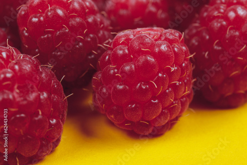Heap of fresh ripe and sweet raspberries on yellow background. Red raspberries. Macro shot.