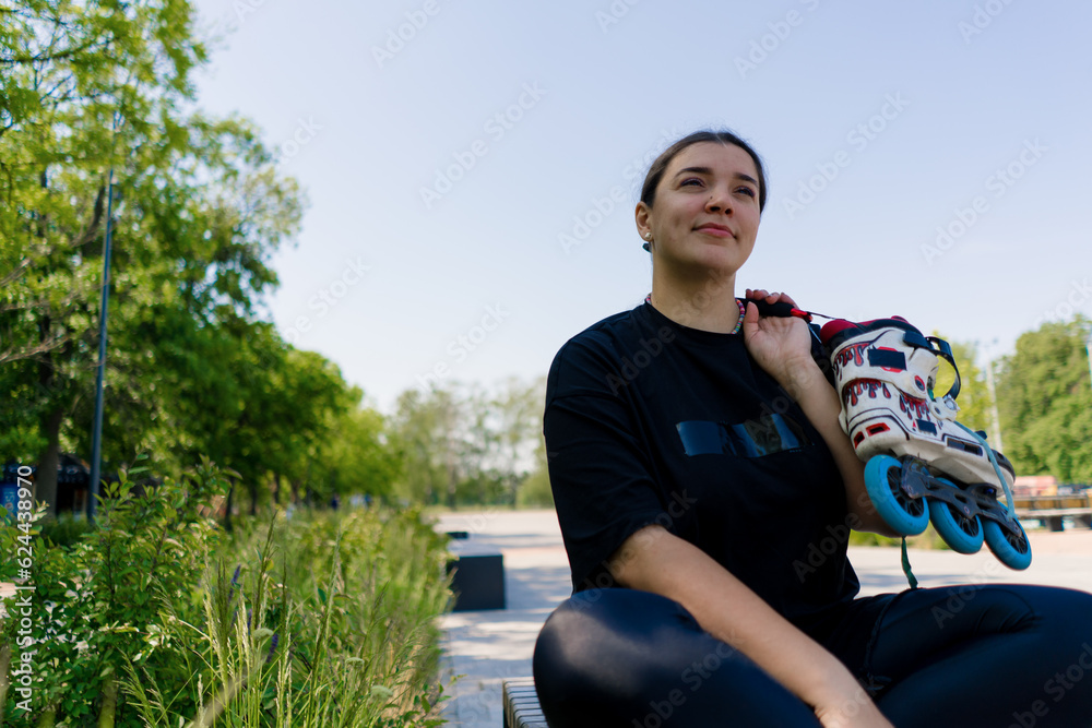 portrait of young smiling hipster girl in skate park holding roller skates in hands before starting skating