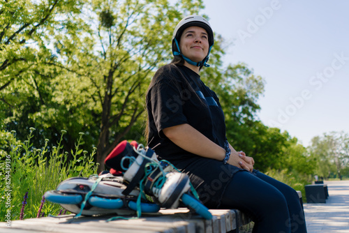 portrait of a young smiling hipster girl in a skate park wearing a protective helmet before starting to skate roller skates in the background