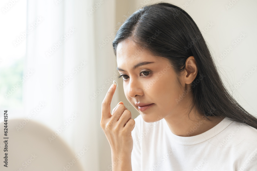 Ophthalmology care, eye sight, vision concept. Asian young woman, female hand holding and putting, wearing soft contact lenses with finger on face, girl looking in mirror at home. Medicine and health. Ophthalmology care, eye sight, vision concept. Asian young woman, female hand holding and putting, wearing soft contact lenses with finger on face, girl looking in mirror at home. Medicine and health.