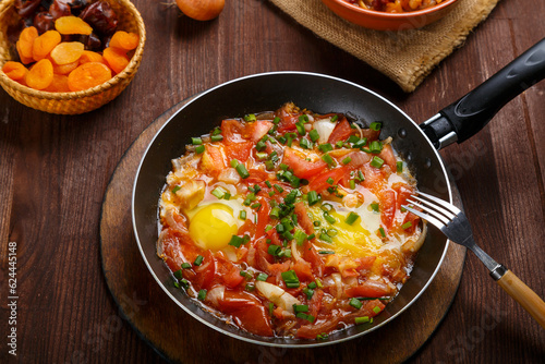 fresh shakshuka in a frying pan sprinkled with green onions on a laid Shabbat table.