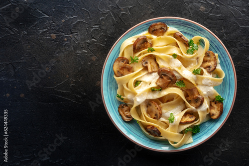 Mushroom pasta, pappardelle with cream sauce and parsley, shot from above on a black stone background, with a place for text