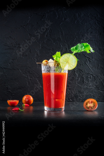 Bloody Mary cocktail with garnish on a black background. A glass of spicy tomato juice with alcohol, lime, celery, pickles, and peppers