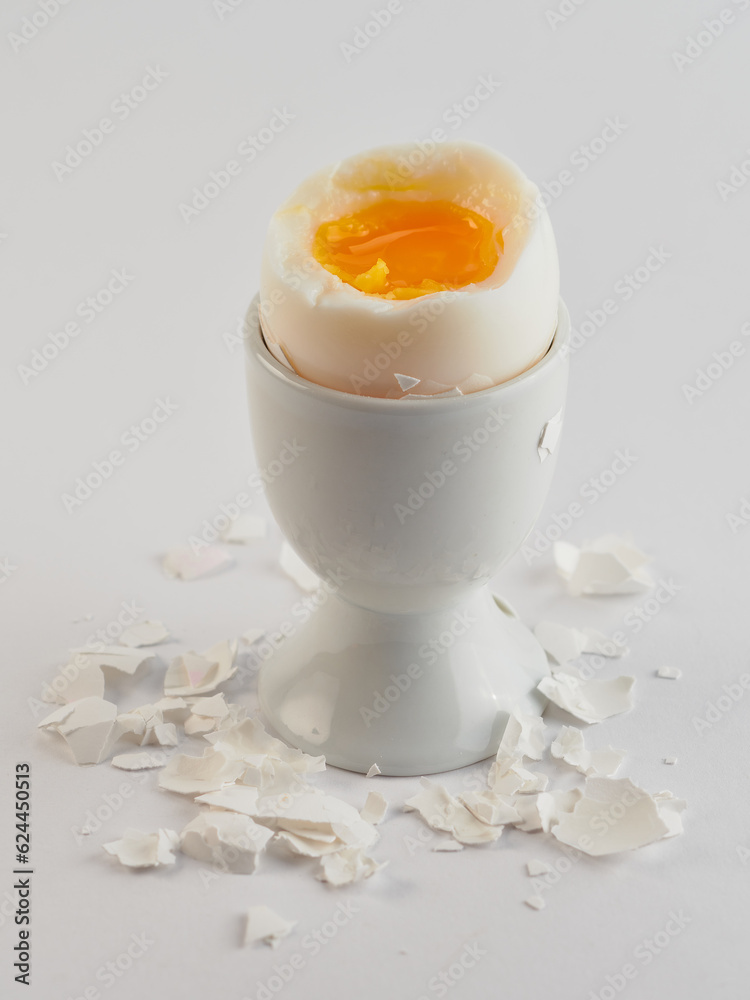 Broken and peeled white egg with runny yolk in a white egg cup Broken and peeled white egg with runny yolk in a white egg cup