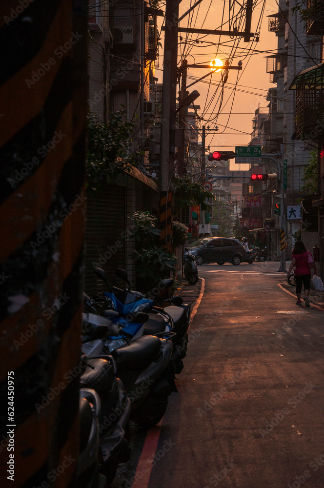 Pedestrians and motor vehicles crowded in the narrow alleyway under the sunset