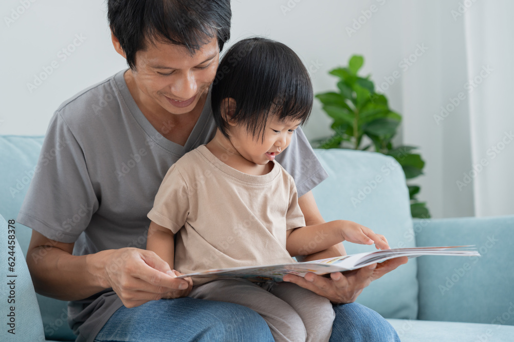 Fototapeta premium Happy Asian father relax and read book with baby time together at home. parent sit on sofa with daughter and reading a story. learn development, childcare, laughing, education, storytelling, practice.