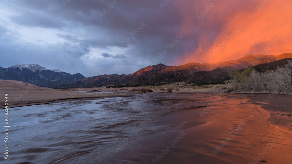 Sunset Medano Creek - A ray of twilight illuminates misty clouds hovering over rolling hills and rushing Medano Creek on a stormy Spring evening. Great Sand Dunes National Park, Colorado, USA.