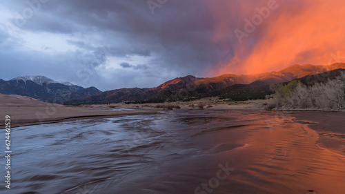 Sunset Medano Creek - A ray of twilight illuminates misty clouds hovering over rolling hills and rushing Medano Creek on a stormy Spring evening. Great Sand Dunes National Park, Colorado, USA.