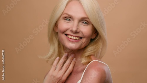 Portrait middle aged happy mature Caucasian woman senior 50s model flirty smiling at camera on beige studio background anti-aging beauty skin care procedures face lifting anti-wrinkle plastic surgery