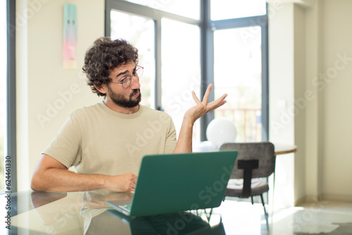 young adult bearded man with a laptop smiling proudly and confidently, feeling happy and satisfied and showing a concept on copy space