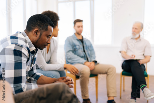 Closeup face of pensive sad african american man discussing alcohol addiction at therapy session. Black male making confession in front of support group people. Concept of mental health, social issues