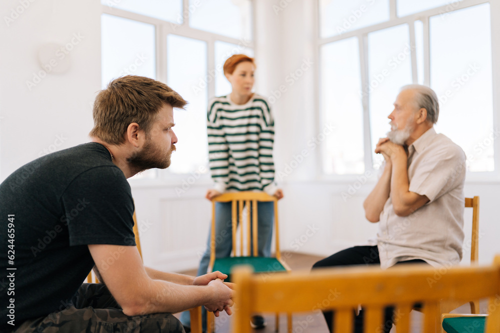 Obraz premium Selective focus of young Caucasian woman standing in front of different ages people. Anxiety stressed female in modern mental health support group session in rehab center. Concept of mental health.