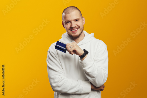 Attractive cheerful man showing credit card for e-commerce, pay cashback, loan, e-banking isolated over yellow background