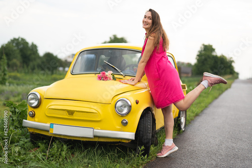 beautiful girl in a pink dress with a bouquet of red roses near a yellow retro car