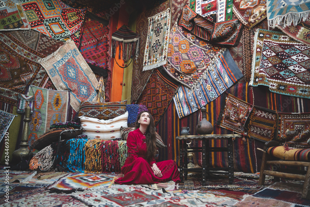 a beautiful girl in a red dress in a traditional turkish interior with many carpets on the wall