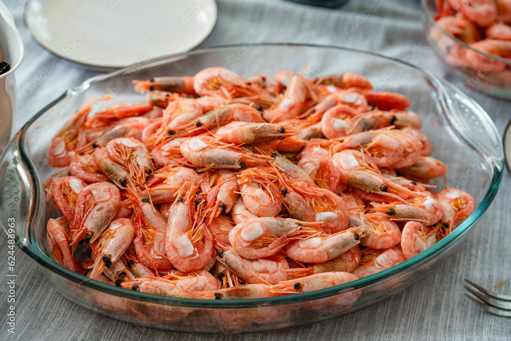 A dish of unpeeled shrimp on a dinner table with plates. Seafood diner. Boiled shrimps. vegetarian dinner, food. A dish of unpeeled shrimp on a dinner table with plates. Seafood diner. Boiled shrimps. vegetarian dinner, food.
